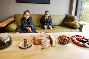 dos hermanas usan bata de baño, se sientan en el sofá y beben té con panecillos. foto