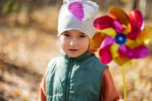 Autumn outdoor portrait of beautiful happy child girl in forest with windmill stick. photo