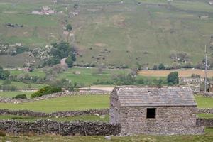 Muro de piedra apilada en seco y edificio de piedra con un cielo nublado yorkshire dales reino unido foto