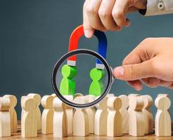 A magnifying glass looks at a magnet pulls green figures of people out of the crowd. Recruiting new workers. Formation of a new business team. Search talented workers with great career potential photo