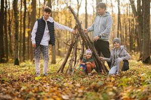 Children with father constructs a house from sticks in autumn forest. photo