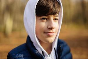 Close up portrait of teen boy in hoodie and sleeveless vest at fall forest. photo