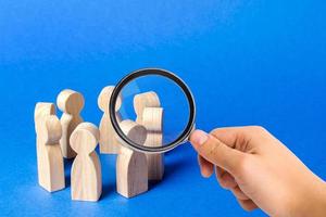 A magnifying glass looks at a people figurines stand in a circle. discussion, cooperation. Meeting at work, negotiating a plan of action. teamwork. Employees briefing. Organization of work processes photo