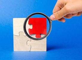 A magnifying glass looks at a red wooden puzzles on a blue background. Individual opinion. Stand out from the crowd. Uniqueness. Divergent views. Different concepts to other people.