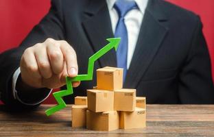 Businessman holding a green arrow up over boxes. Boost sales rate. Increasing production of goods, expanding export opportunities, finding markets. Tactics and strategy, marketing. Value added goods photo