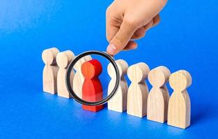 A magnifying glass looks at a red figure person comes out of people line. Leadership qualities, talented employee. HR is looking for new employees, choice among candidates. A suitable candidate photo