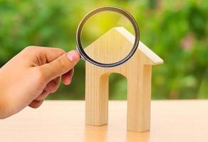 A magnifying glass looks at a wooden figure of a house with a large doorway. Home, Affordable housing, residential building. concept of buying or selling real estate, rent, investment and construction photo