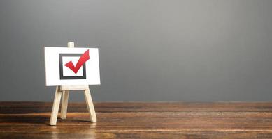 Easel with red voting tick. Checkbox. Democratic elections, referendum. Right to choose, change of power. Checklist verification, self-discipline. Necessary quality criteria, skills, approval symbol photo