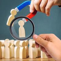 A magnifying glass looks at a magnet pulling wooden figures of people from the crowd. Recruiting new workers, headhunters. Formation of a new business team of applicants. Personnel Management. photo