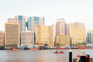 Dubai, UAE, 2022 - vintage boats and ships on river by beautiful new buildings in Dubai creek district in summer photo