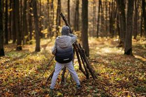 Boy constructs a house from sticks in autumn forest. photo