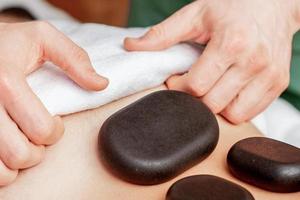 masaje con piedras en la espalda del hombre. foto