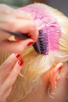 Hairdresser dyes hair of young woman in pink color photo