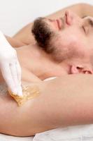 Cosmetologist applying wax paste on male armpit photo