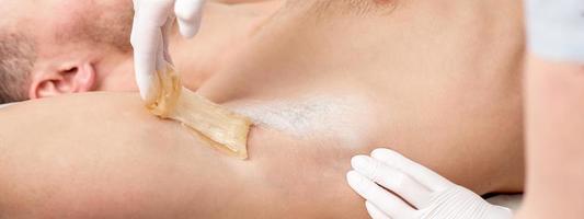 Cosmetologist applying wax paste on male armpit photo