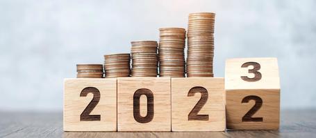 volteando el bloque de 2022 a 2023 años con pila de monedas. conceptos de dinero, presupuesto, impuestos, inversiones, finanzas, ahorros y resolución de año nuevo foto