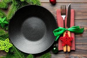 Top view of New Year dinner on festive wooden background. Composition of plate, fork, knife, fir tree and decorations. Merry Christmas concept photo