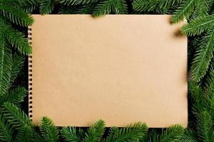 Top view of notebook made of craft paper decorated with a frame made of fir tree on wooden background. New Year time concept photo