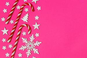 Christmas candy cane lied evenly in row on pink background with decorative snowflake and star. Flat lay and top view photo