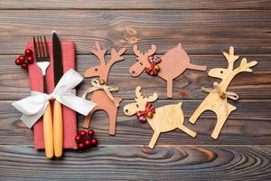 Top view of holiday objects on wooden background. Utensils tied up with ribbon on napkin. Close up of christmas decorations and reindeer. New year dinner concept photo