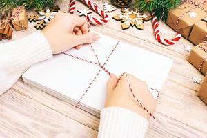 Many envelopes tied with rope. Close-up top view of famale hands with envelope. Pine cones and christmas decoration on old wooden table, desk. Toned photo