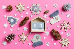 vista superior del calendario de madera, juguetes navideños y decoraciones sobre fondo de navidad rosa. el primero de enero. concepto de tiempo de año nuevo foto