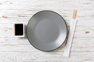 Empty grey round plate with chopsticks for sushi and soy sauce on wooden background. Top view with copy space photo
