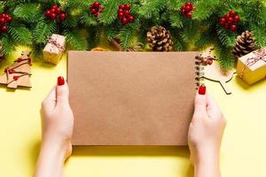 Top view of female hand making some notes in noteebok on yellow background. New Year decorations and toys. Christmas time concept photo