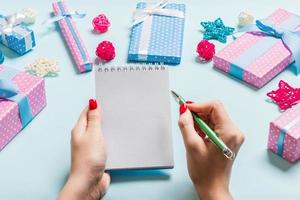 Top view of female hand making some notes in noteebok on blue background. New Year decorations and toys. Christmas time concept photo