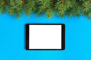 Tablet with blank screen on the blue pastel color background. Top view with christmas decor photo