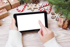 Christmas background female hands uses opened tablet with copy space on rustic wooden table covered with Christmas decoration. top view, flat lay photo