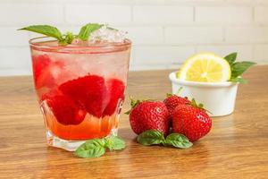 A refreshing summer drink with ice, strawberries and lemon on a wooden background. The concept of fruit drink. photo