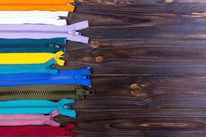 Multicolored zippers are laid out on a wooden table photo