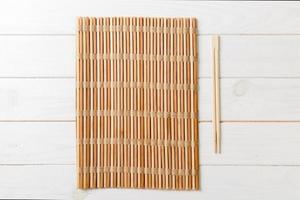 two sushi chopsticks with empty bamboo mat or wood plate on wooden Background Top view with copy stace photo