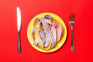 Top view of heap of colorful measuring tapes in plate on red background. Diet concept with copy space photo