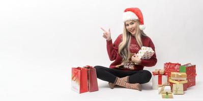 Portrait of happy Caucasian young woman in santa claus hat with gift box and shopping bags over white background photo
