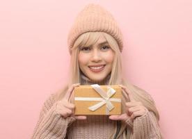 Portrait of Caucasian young woman wearing sweater holding gifts box  over Pink background photo