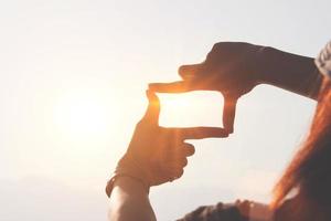 concepto de planificación y visión del comienzo del año nuevo, manos de mujer haciendo gestos de marco para encontrar el foco al atardecer, mujer buscando perspectiva para capturar el significado de un próximo objetivo claro. foto