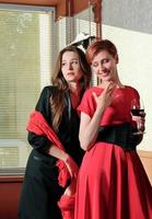 Portrait of elegant young women with vine glasses at celebration party. black and red outfit. photo