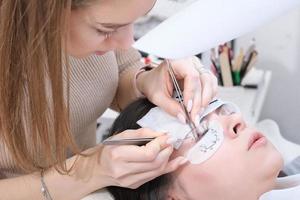 Master applies lash dye to eyelashes. Close-up of beauty model's face during lash extension procedure. Eyelash Care Treatment. eyelash lamination and extension. photo