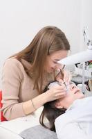 mujer joven esteticista haciendo procedimiento de pestañas postizas para un cliente. toma vertical del procedimiento de extensión de pestañas foto