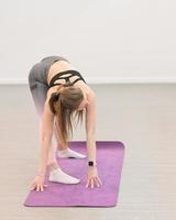 young slim woman wearing top and leggings doing bends on a yoga mat. pilates and stretching exersice in a gym. vertical. photo