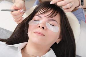 woman client lying in beauty salon redy to eyelash extension procedure. eyepatches under woman's eyes photo