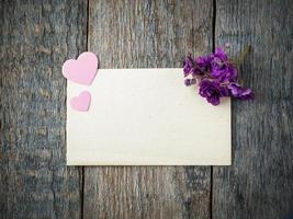 corazón de papel y flores de violetas en una vieja hoja de papel sobre fondo de madera rústica foto