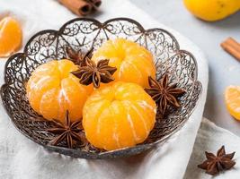 Fresh mandarins in a plate with fir tree branches, star anise cinnamon on gray background photo