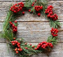 Christmas wreath of pine branches and red Rowan on wooden background. Copy space. photo