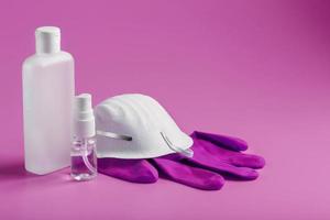 kit de protección antivirus sobre fondo rosa, máscara, guantes de goma, botellas de desinfectante para manos, gel antiséptico. aislar