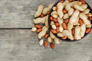 Roasted peanuts in the shell and peeled in a cup, against a gray wooden table photo