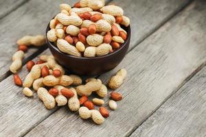 Roasted peanuts in the shell and peeled in a cup, against a gray wooden table photo