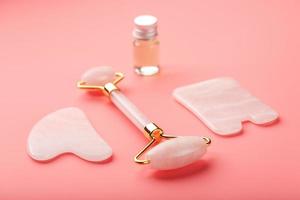 herramienta de masaje gua sha hecha de rodillo de cuarzo rosa natural, piedra de jade y aceite, sobre un fondo rosa para el cuidado de la cara y el cuerpo. parte de la medicina tradicional china foto